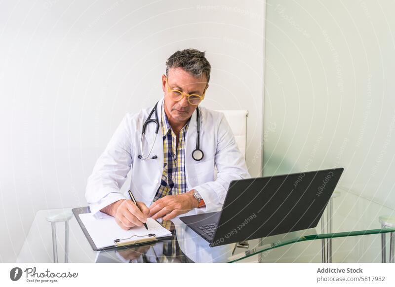 Male doctor working on laptop and clipboard in medical office Analyzing Healthcare And Medicine Occupation Professional Occupation cardiac check clinic computer