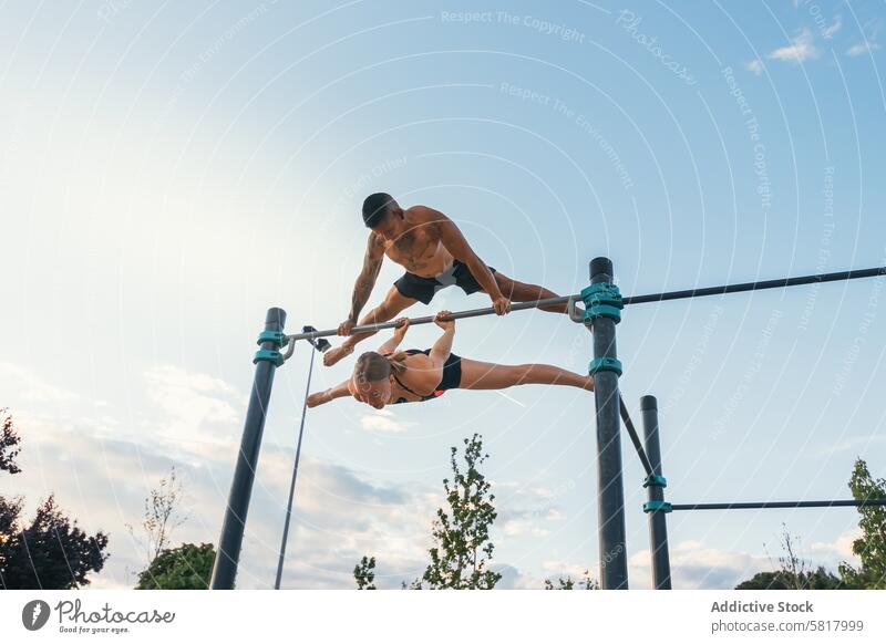 couple training together in a calisthenics park. doing back lever and straddle planche. workout exercise fitness outdoor woman young sport summer bodyweight