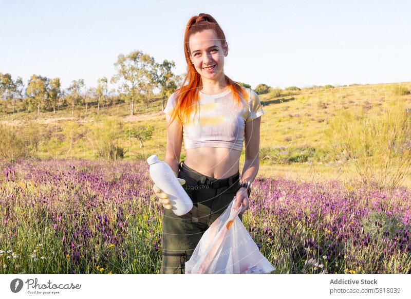 Young woman engaging in environmental cleanup in a field conservation garbage young orange hair bottle trash bag outdoors nature green volunteer activity