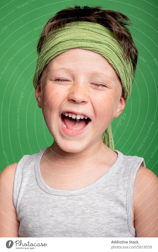Cheerful young boy laughing with eyes closed in studio child cheerful happy joy studio shot green background headband male fun smile happiness youth tank top
