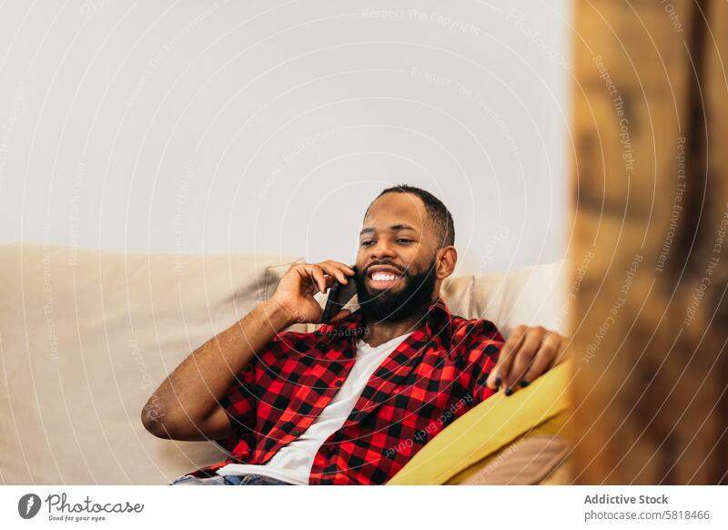 African american man making a call with smartphone relaxed at home sofa black couch african american mobile technology happy communication cheerful adult