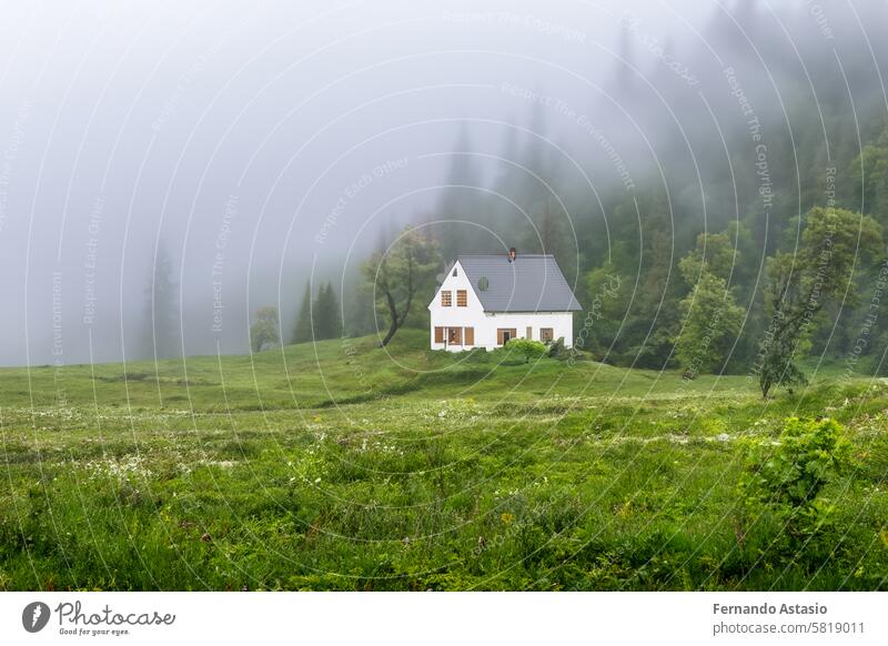 Isolated house in the mountains, beautiful typical northern European house in a lush, green landscape with fog. Beautiful summer landscape with green meadows and house in the mountains.