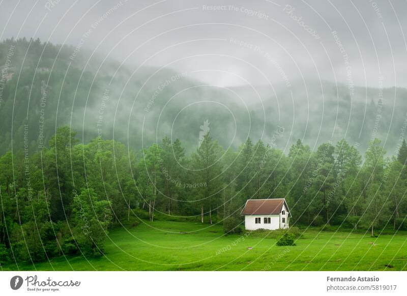 Isolated house in the mountains, beautiful typical northern European house in a lush, green landscape with fog. Beautiful summer landscape with green meadows and house in the mountains.