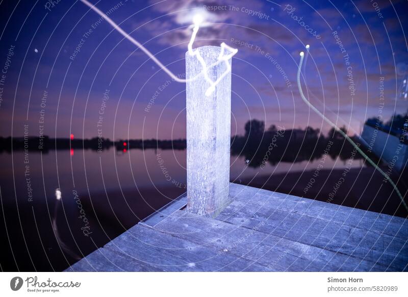 Mooring post of a wooden jetty in the nocturnal surroundings of a lake with blurred celestial bodies wooden walkway Night bank Long exposure stake