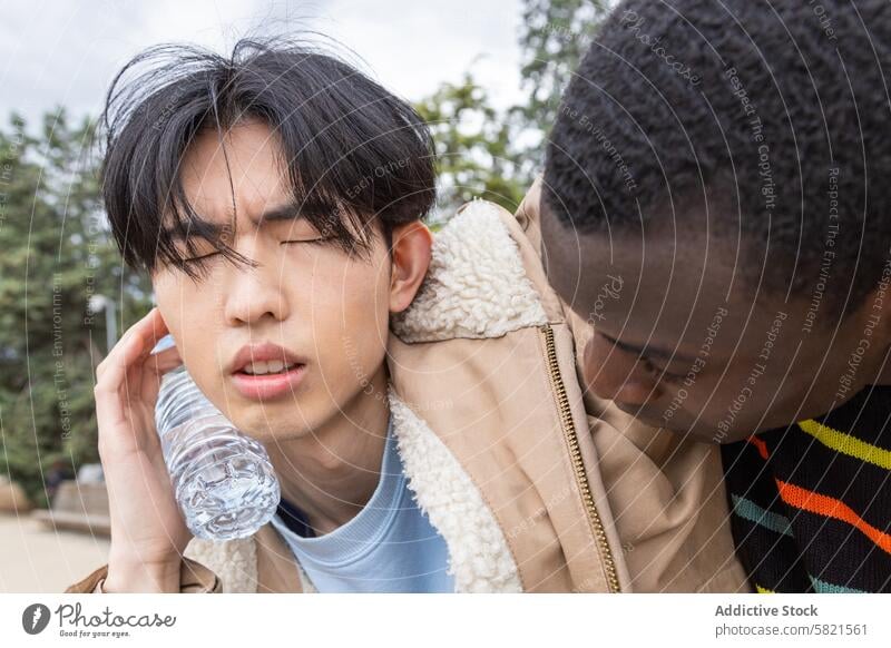 Young man experiencing hypoglycemia symptoms outdoors dizzy unwell assistance friend asian african male water bottle concern health medical emergency helping