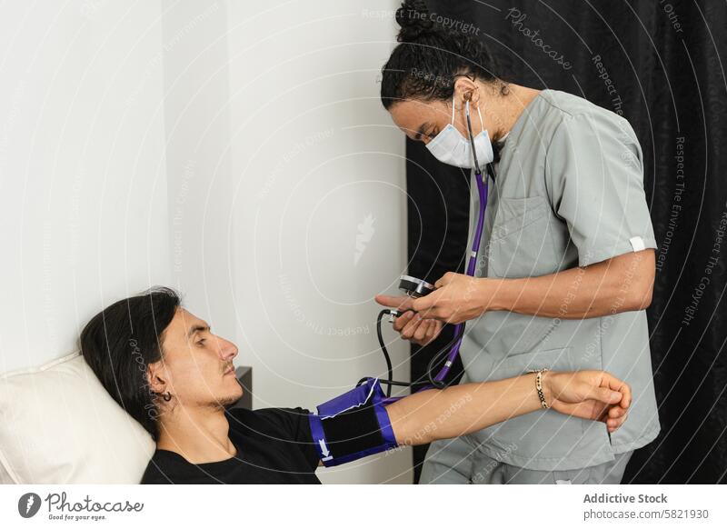 Nurse checking patient's blood pressure during medical examination nurse health monitoring clinical male lying gurney healthcare mask uniform gray stethoscope