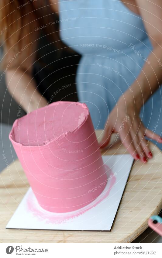 Decorator icing a pink cake on a wooden board decorator confectionery apron blue art baking decorating dessert pastry sugar craft kitchen cooking culinary