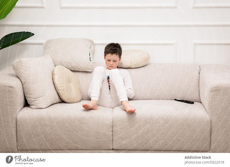 Young boy immersed in reading at home child book couch sitting pajamas focused calm indoor leisure activity literacy learning education cross-legged alone