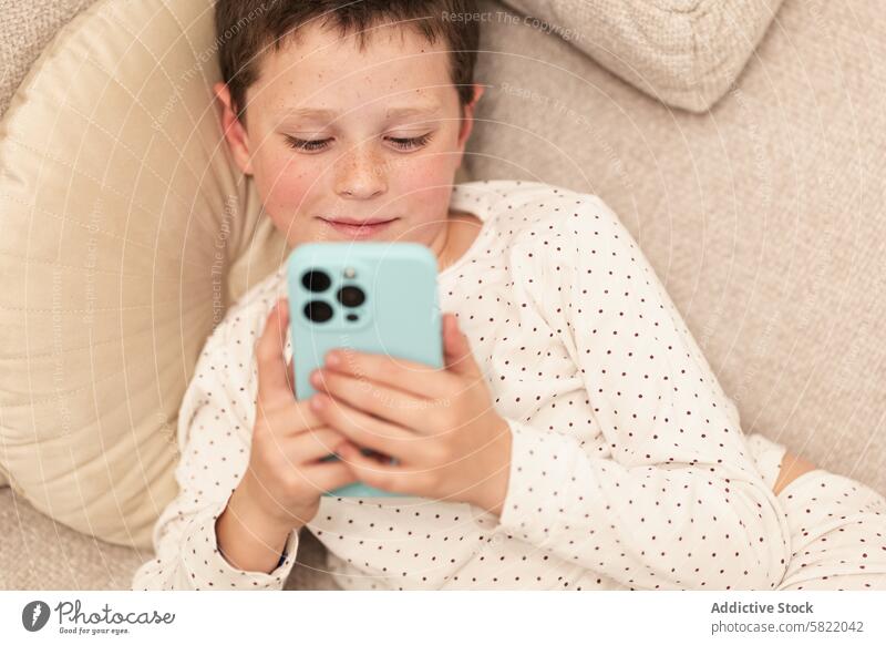 Boy relaxing at home using smartphone boy technology relaxation lying down comfortable leisure focused smile gentle eyes downward young screen digital