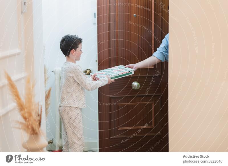 Young boy receiving a pizza delivery at home pajamas door excitement accepting box young indoor food smile casual comfort childhood leisure activity house