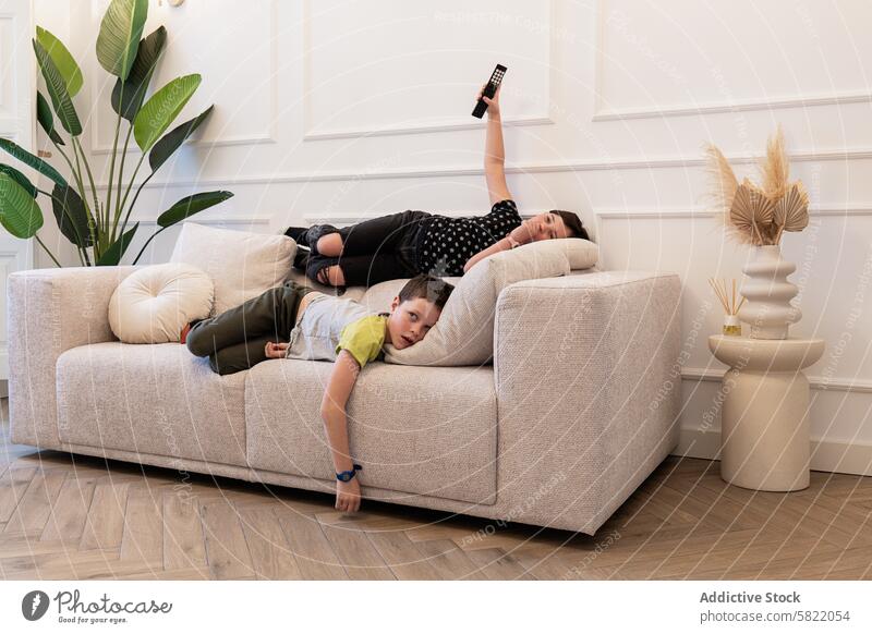 Kids relaxing on sofa with remote control in hand child boy girl home lounge looking at camera looking away casual comfort indoor living room leisure sibling