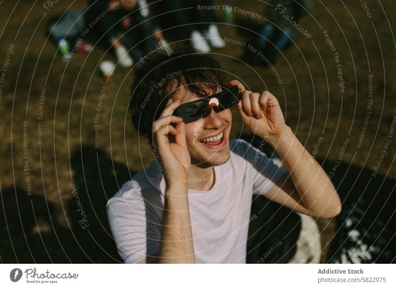 Young man excitedly using solar eclipse glasses outdoors young park friend group cheerful nature gathering sunlight daytime leisure activity watching event