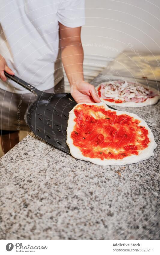 Preparing handmade pizza dough in a pizzeria tomato sauce pizzaiolo preparation peel kitchen cooking food italian cuisine chef anonymous faceless restaurant