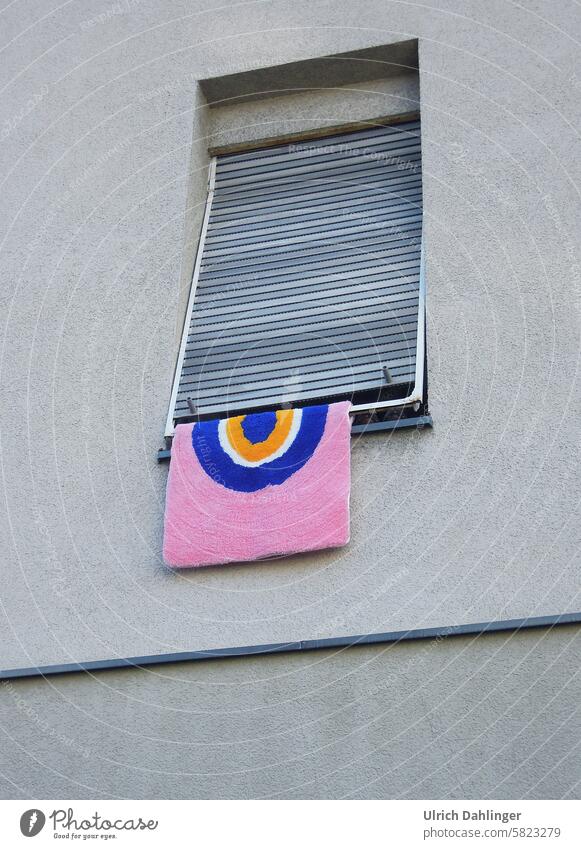 pink carpet with a yellow/white/blue ring pattern hangs out of a window with an almost closed shutter Colour Contrast Window Pattern Carpet Structures&Shapes