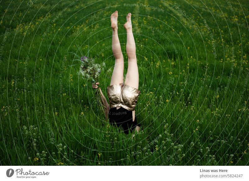 This green grass meadow is a comfortable place for a gorgeous girl to be upside down. With her pretty long legs and a bouquet of flowers in her hands, she is feeling just fine. Spring has begun, and so has the odd stuff.