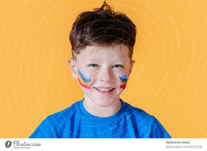Young boy with colorful face paint on a yellow background smile happy child blue shirt painting young cheerful expression joy fun kid vibrant portrait