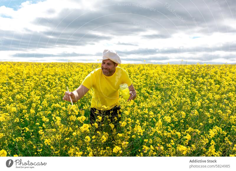 Man in yellow shirt painting flowers in blooming field farmer rapeseed agriculture cloudy sky male planting inspecting vibrant nature outdoor rural farmland