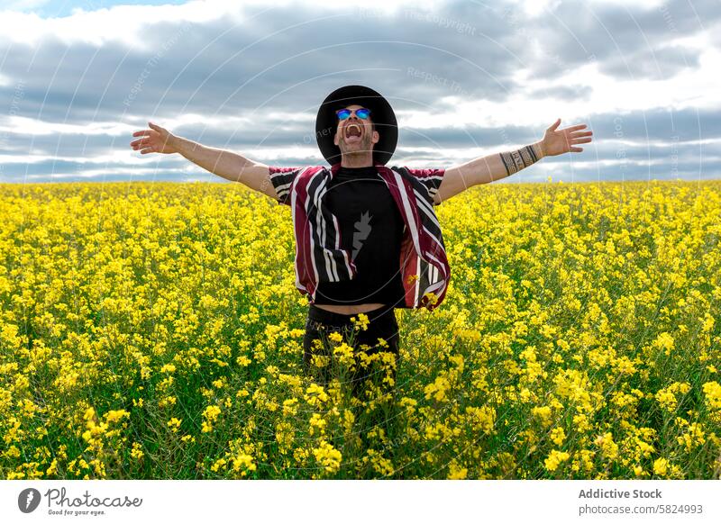 Man celebrating in a vibrant yellow rapeseed field man flower joy freedom celebration happiness outstretched arms cloudy sky nature outdoor spring blooming