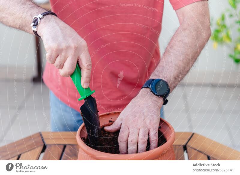 Man planting in a terracotta pot on a sunny terrace man trowel green soil gardening outdoor hobby care dirt hand wristwatch smartwatch red t-shirt urban