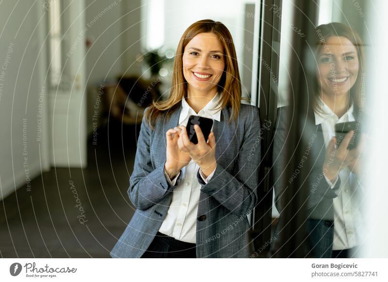 Smiling Businesswoman in Modern Office Holding Smartphone Enjoying a Successful Work Day businesswoman smiling office smartphone professional modern corridor