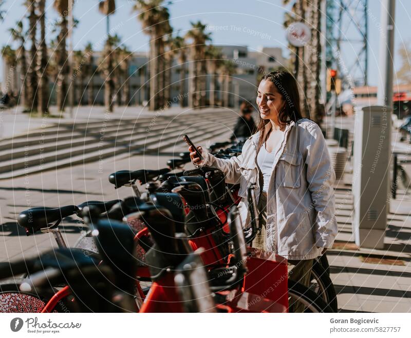 A serene spring afternoon in Barcelona with a smiling woman renting a bicycle scanning public phone ecological biking bike application city life barcelona