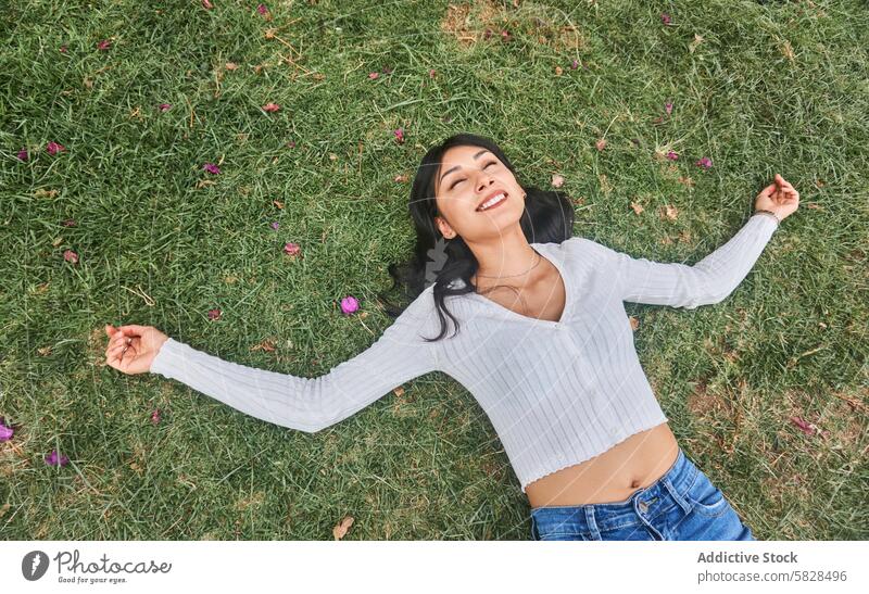 Young Woman Enjoying a Relaxing Moment in Nature woman relaxation park nature grass lying down field petals pink scattered outdoor leisure happiness casual