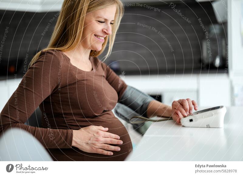 Pregnant woman measuring her blood pressure at home pregnancy pregnant adult anticipation awaiting baby belly birth body care caucasian child expectant
