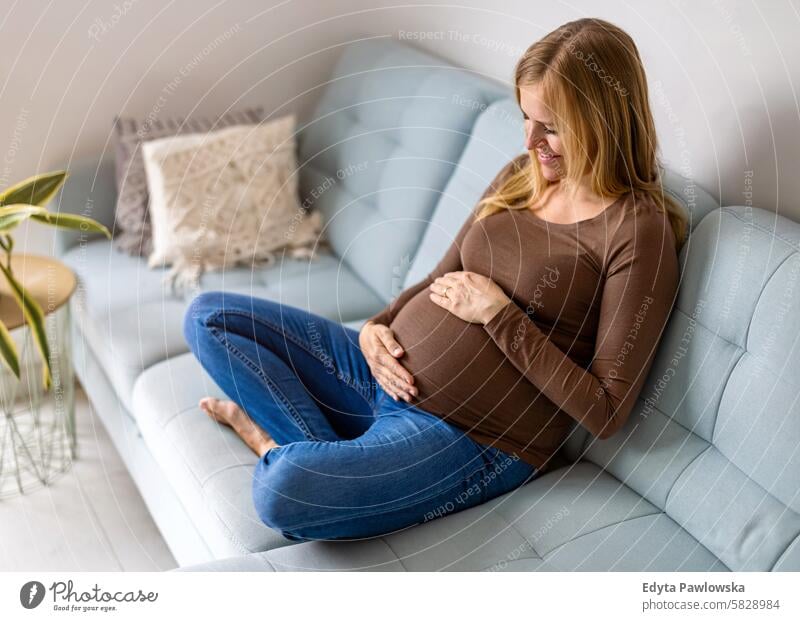 Pregnant woman touching her belly, relaxing on sofa at home pregnancy pregnant adult anticipation awaiting baby birth body care caucasian child expectant
