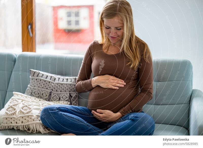 Pregnant woman touching her belly, relaxing on sofa at home pregnancy pregnant adult anticipation awaiting baby birth body care caucasian child expectant