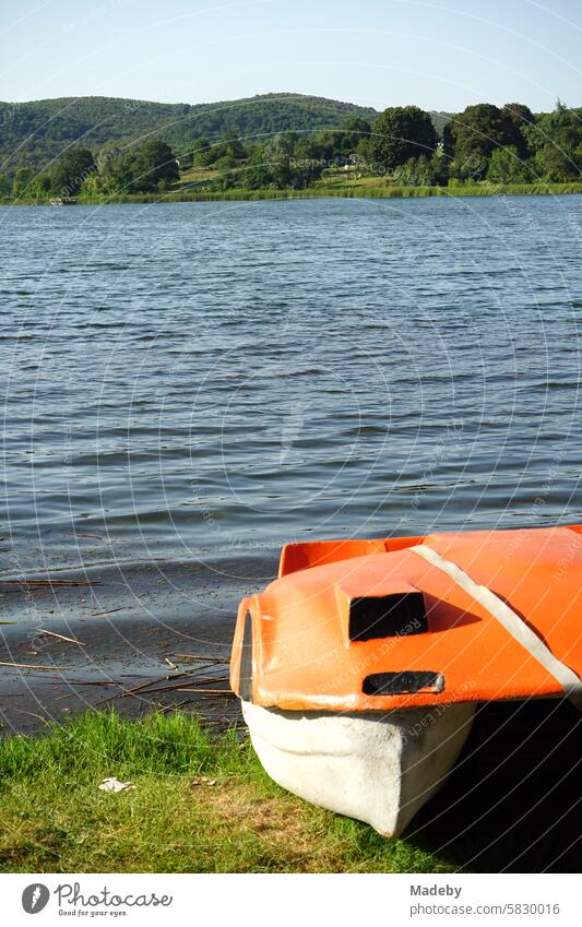 Old pedal boat made of plastic in bright orange on the shore in summer against a blue sky in the sunshine at Poyrazlar Gölü near Adapazari in the province of Sakarya in Turkey