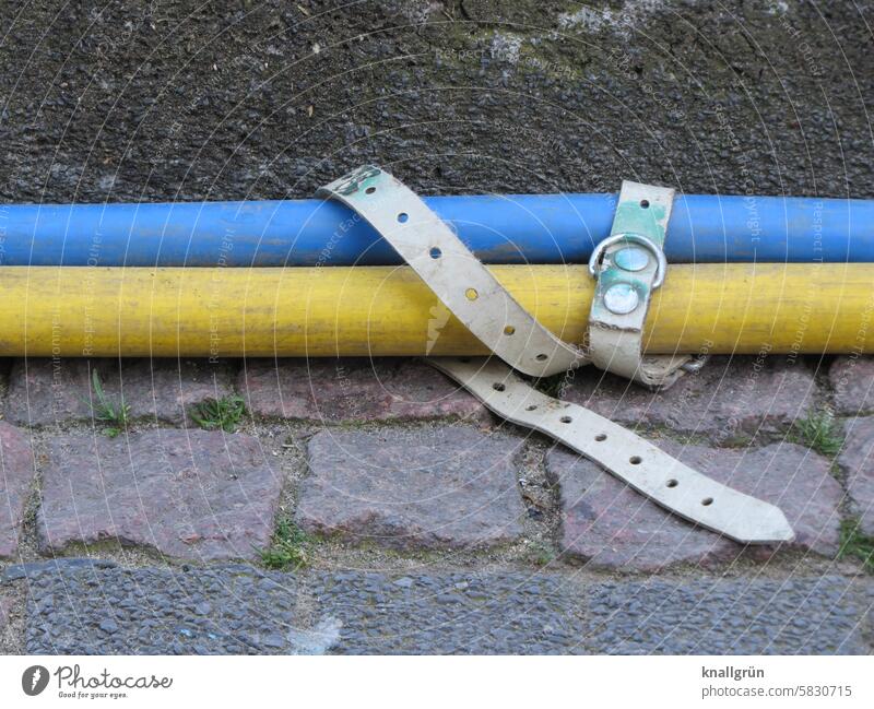 Loose binding Cable Fastening Attachment Belt White Blue Yellow Gray Side by side Close-up Colour photo Lie Paving stone Curbstone Exterior shot Day