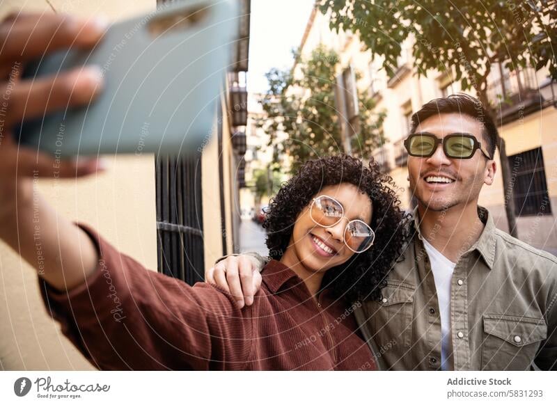 Multiethnic couple taking a selfie in a vibrant street in Madrid madrid spain travel tourism vacation smile sunglasses happiness urban city love relationship
