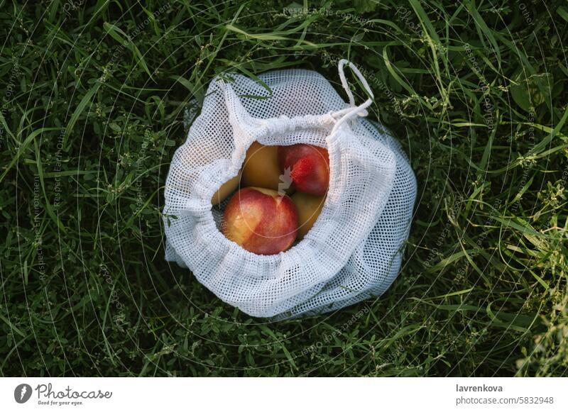 Reusable mesh bag with nectarines and peaches on green grass, zero waste grocery concept lifestyle healthy food organic recycle reusable natural environment