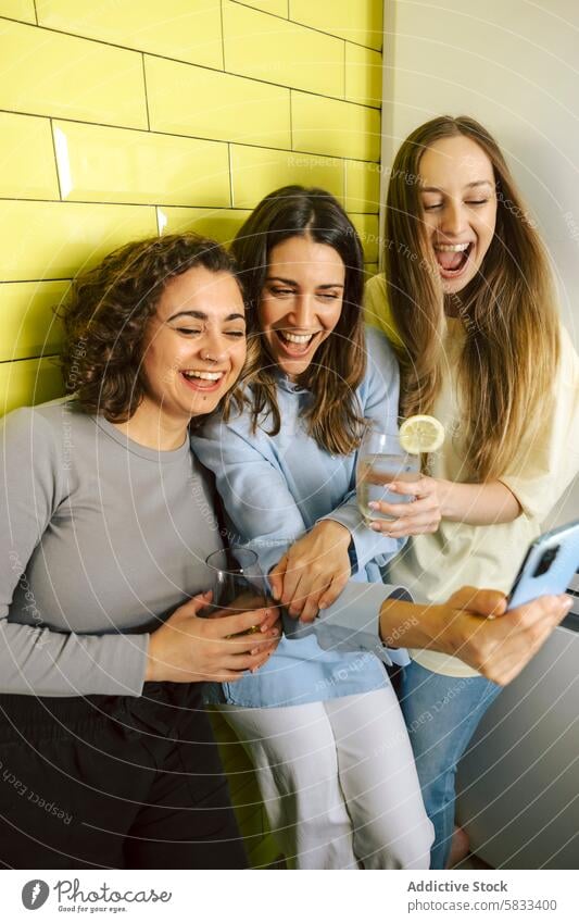 Joyful friends sharing a moment of laughter indoors women home play drink good time gender each other down selfie cheerful gathering yellow background enjoyment