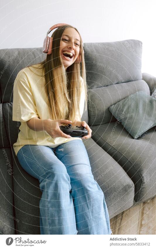 Joyful woman playing video games on couch at home gaming happy headphones controller smile cheerful entertainment leisure young female joy fun laughing sitting