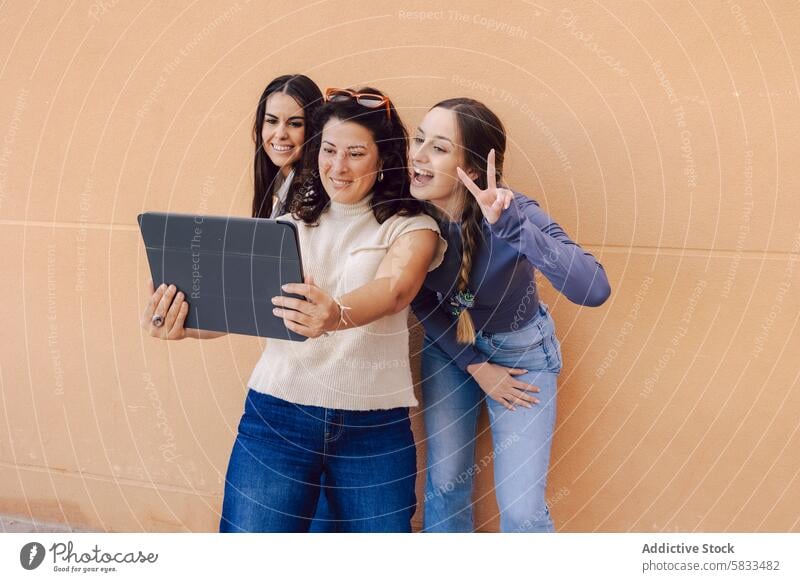 Women sharing a moment with a tablet women interaction technology happiness friendship smile digital orange wall casual clothing joy connectivity online social