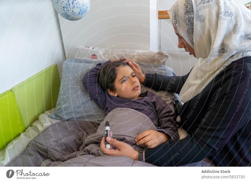 Muslim mother caring for son with hypoglycemia at home care muslim ethnic concern illness touch forehead hijab family arab hispanic healthcare bed bedroom sick