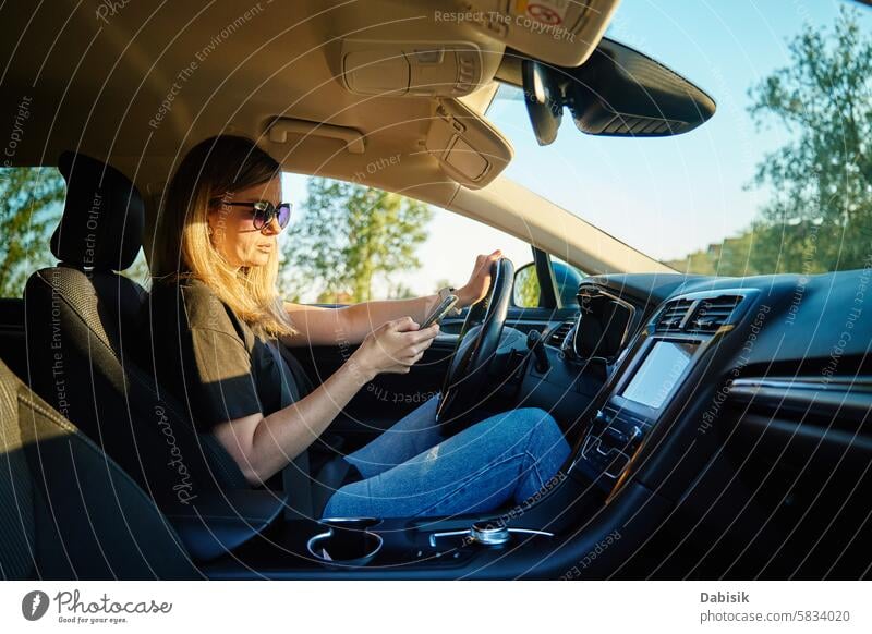 Woman Using Smartphone While Driving in a Car woman smartphone car driving sunglasses driver safety distraction road vehicle afternoon sunny seat device