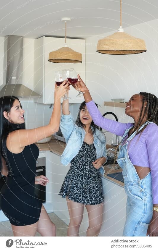 Three young women toast with red wine in a modern kitchen woman glass celebration happy joy contemporary stylish friendship gathering cheers social party drink