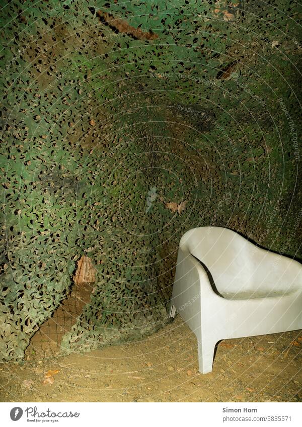 white plastic armchair in front of a camouflage net Armchair Hiding place temporise Hide Sit Camouflage disguised Net dubious opaque Storage Green Mysterious