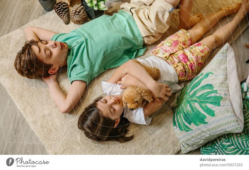 Top view of two children with closed eyes relaxing lying over rug in cozy indoor with warm ambient. relaxation carpet resting serene tent home playful