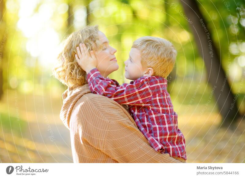Close-up portrait of a mother and son during a walk in the autumn park. Woman holds her toddler son in her arms and hugs him tenderly. boy mom comfort embrace