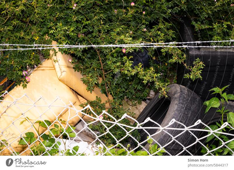 Pile of garbage behind a fence with barbed wire, overgrown by bushes Trash mountain of rubbish Disposal Fence Environmental pollution waste impurity Barbed wire