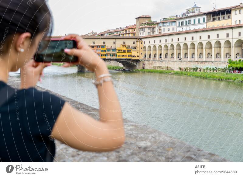 Young photographer taking a picture of the Vecchio bridge in Florence with a smartphone mobile tourist photographing Vecchio Bridge city Italy girl woman young