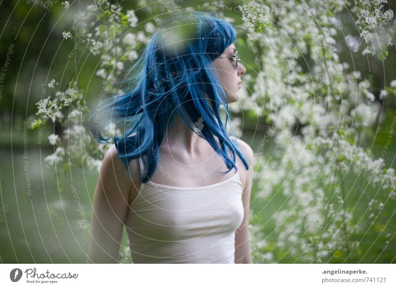 Woman with blue hair stands in profile under a tree with white flowers, she gives her head to the right and the hair flies with Blue Wig Blossom Summer Sun