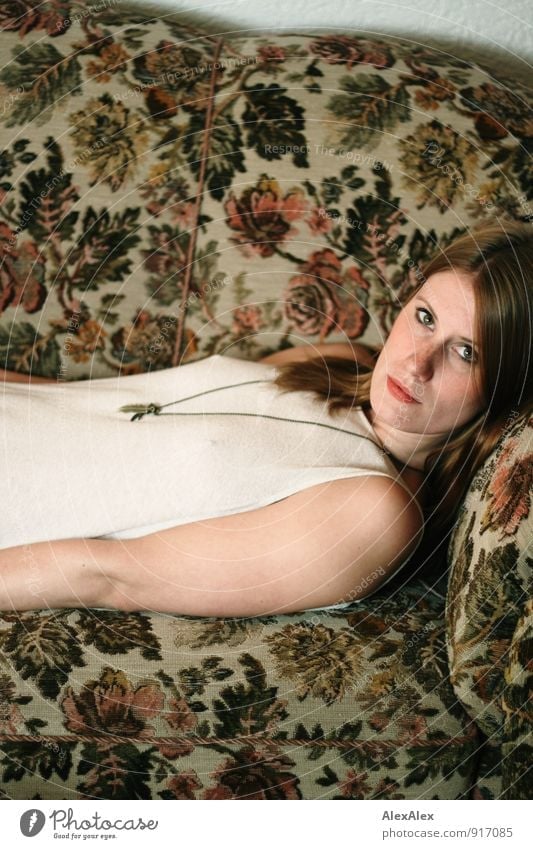 Young, redheaded woman lies on a flowered sofa and looks sideways into the camera Adventure Flat (apartment) Sofa Leaf Pattern Young woman Youth (Young adults)