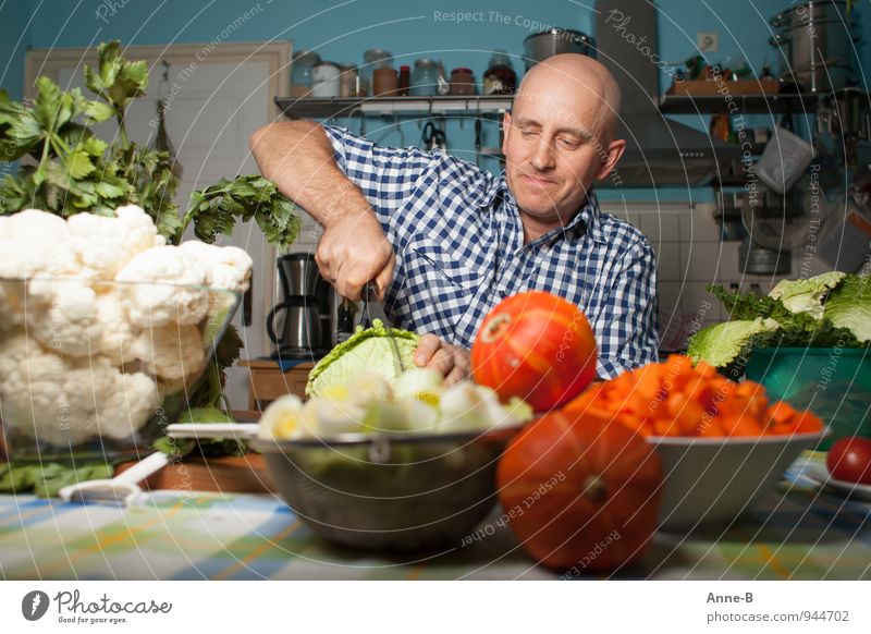 A man in a check shirt is cutting a savoy cabbage in the kitchen. Around him on the table is a lot of vegetables. Vegetable Soup Stew Vegetarian diet Crockery